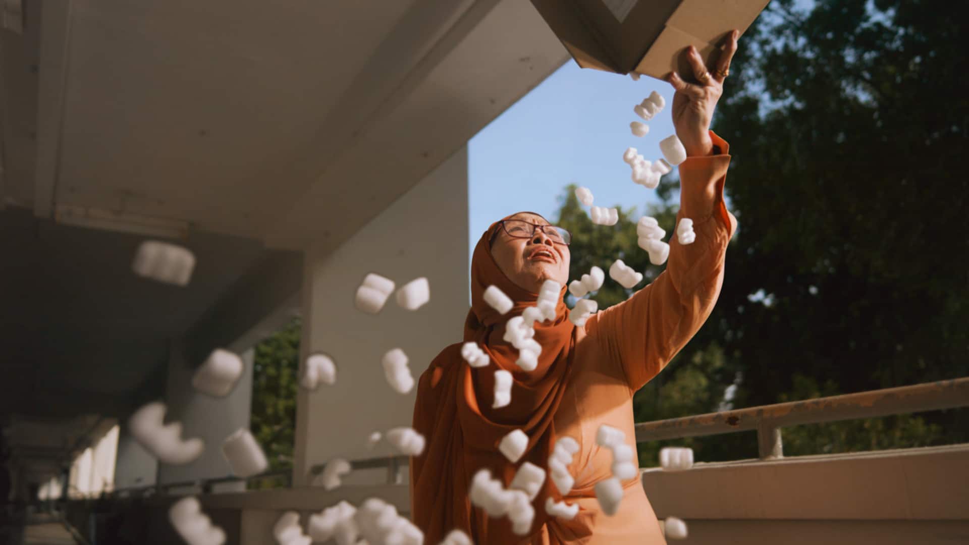 Elderly Muslim woman in an orange hijab tossing packing peanuts